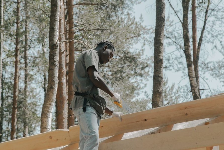 A construction worker sawing wood on a building project outdoors in a forest setting