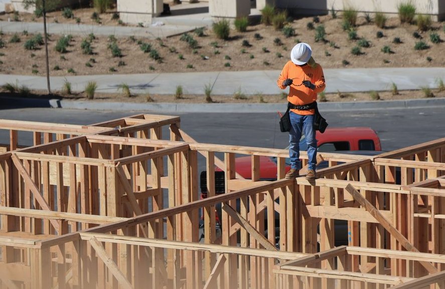 A construction worker on a wooden frame checks a device at a building site